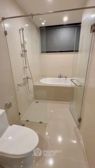 Modern bathroom with glass shower and bathtub, sleek fixtures, and neutral tiles.