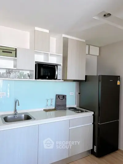 Modern kitchen with sleek cabinetry, stainless steel sink, and black refrigerator in a compact layout.