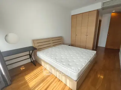 Spacious bedroom with wooden flooring and ample natural light, featuring a comfortable bed and built-in wardrobe.