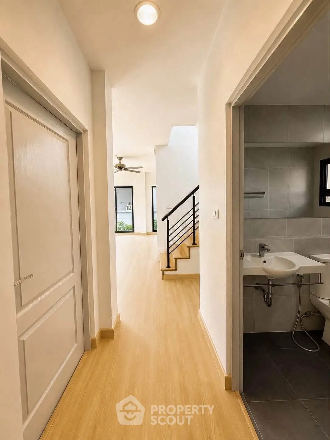 Modern hallway with wooden flooring leading to a bright living area and a compact bathroom.