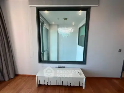 Modern interior with large window and elegant chandelier reflection, featuring sleek wooden flooring and minimalist furniture.