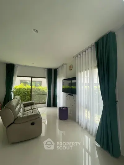 Modern living room with sleek leather sofa and large windows offering lush garden views.