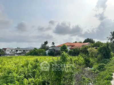 Expansive green landscape with residential houses under a cloudy sky, ideal for development.
