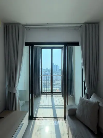 Modern living room with large windows and city view, featuring elegant curtains and cozy seating.