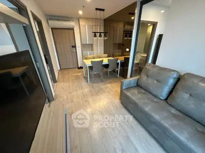 Modern living room with sleek furniture and open dining area, featuring stylish lighting and wooden flooring.