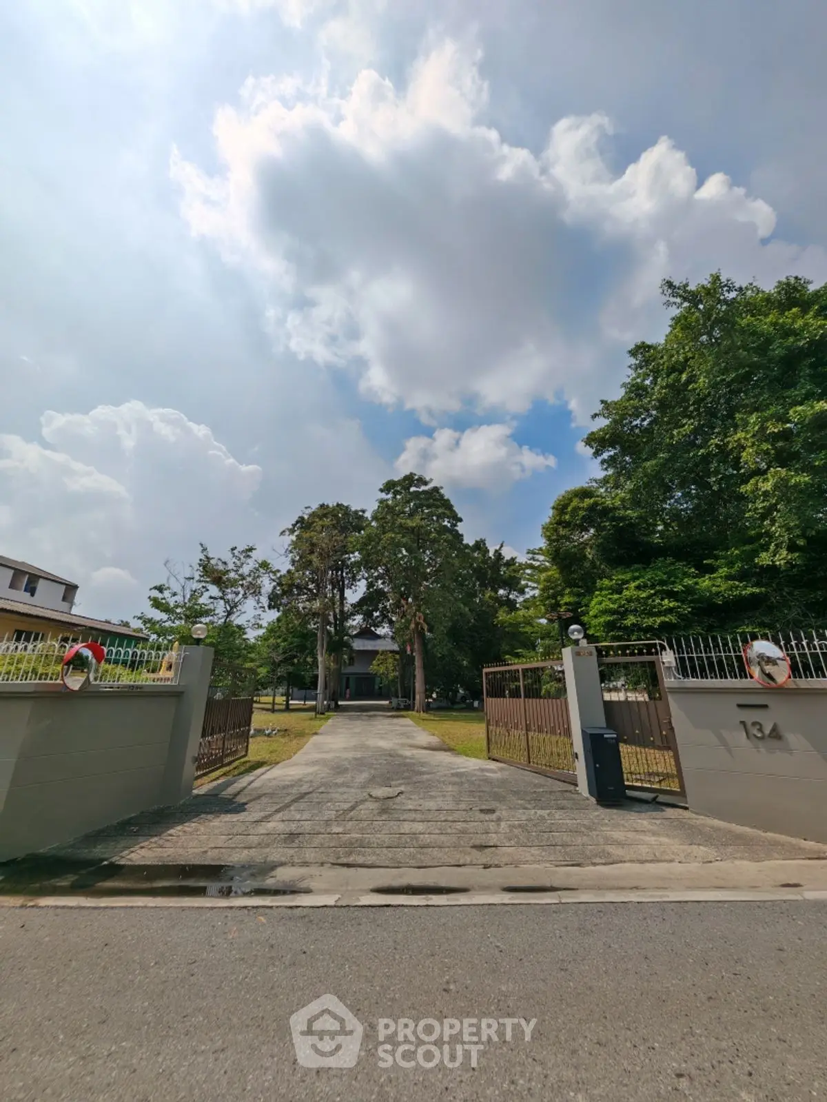 Spacious property entrance with lush greenery and clear sky, ideal for serene living.