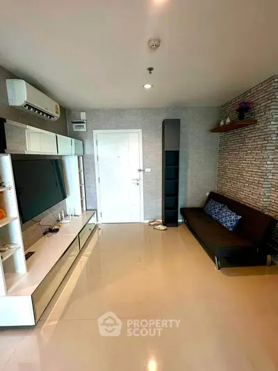 Modern living room with sleek furniture and stylish decor, featuring a large TV and air conditioning.