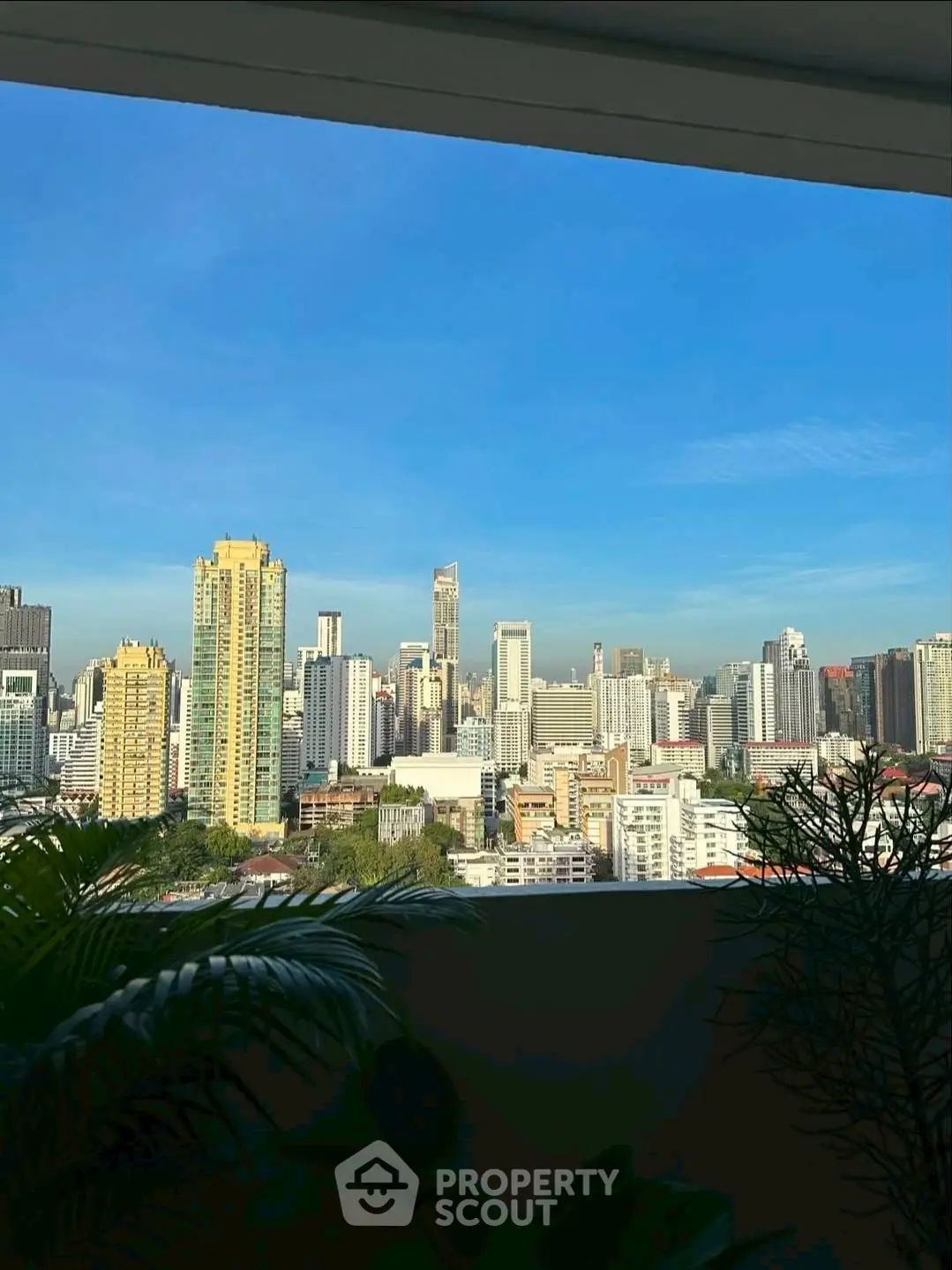 Stunning city skyline view from a high-rise balcony with lush greenery.