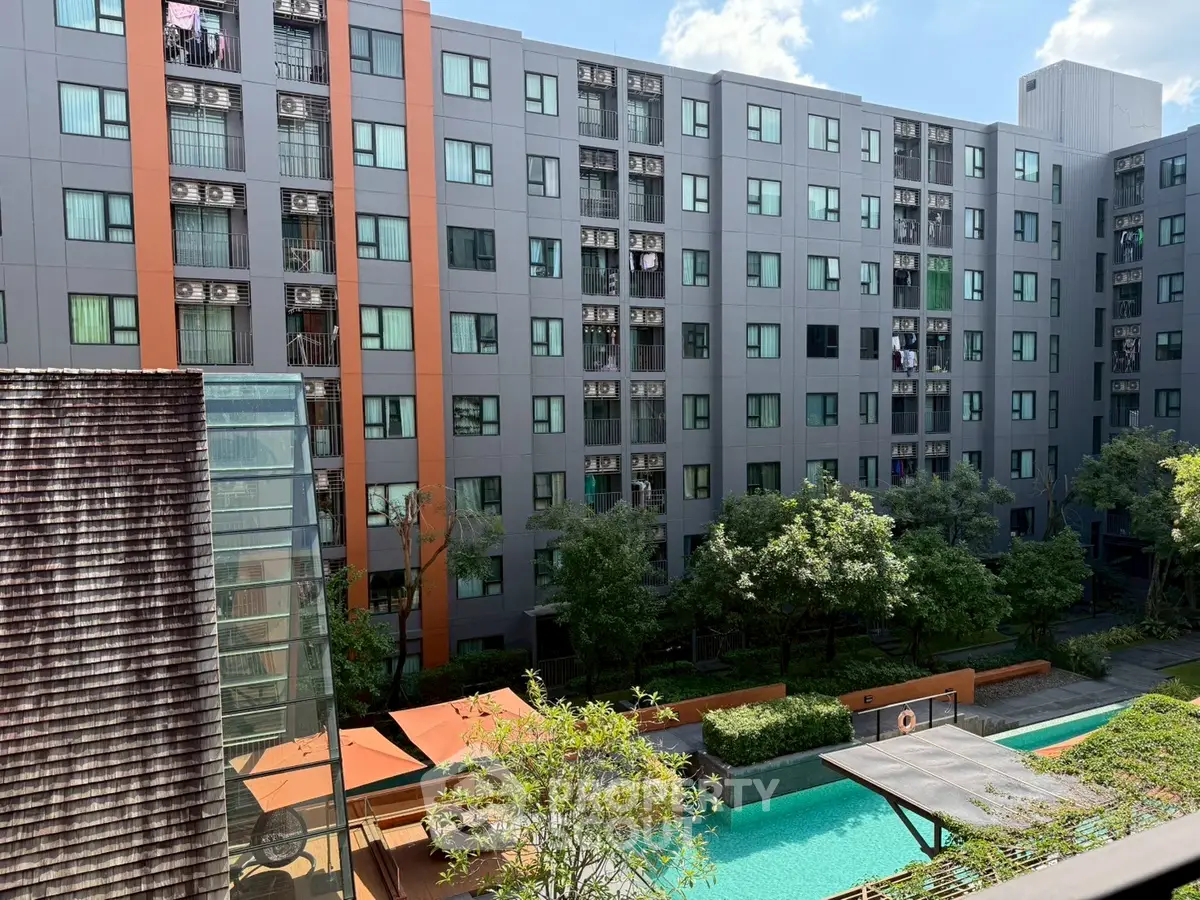 Modern apartment building with pool and lush greenery under a clear blue sky.
