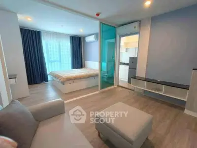 Modern studio apartment with open layout, featuring a cozy living area and bedroom separated by glass partition.