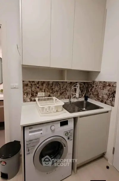 Modern kitchen with washing machine and sleek cabinetry in compact layout.