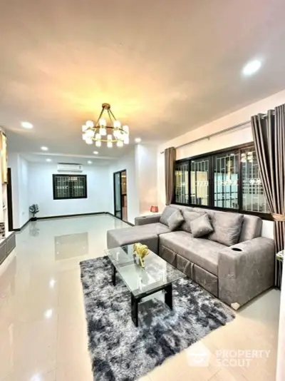 Spacious and elegantly furnished living room with glossy tiled flooring, plush grey sectional sofa, and modern lighting fixtures, creating a luxurious and inviting atmosphere.