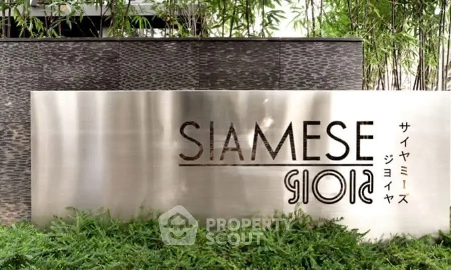 Elegant entrance sign of Siamese Gioia surrounded by lush greenery, showcasing modern architectural design.