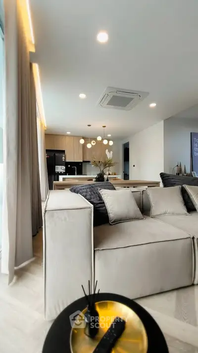 Modern living room with open kitchen, featuring elegant lighting and contemporary furniture.