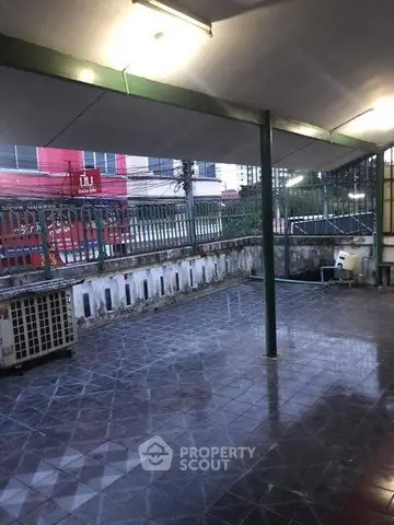 Spacious covered outdoor area with tiled flooring and green metal framework.