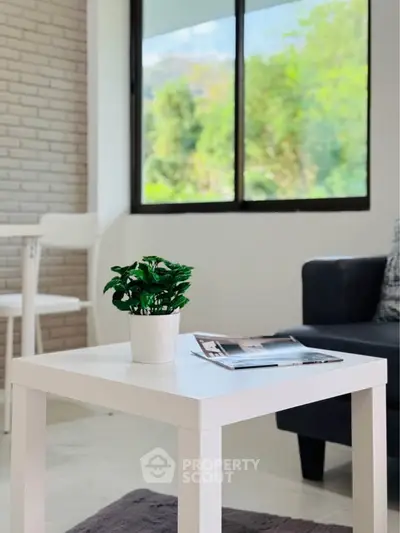 Modern living room with stylish white table and lush green view through large window.