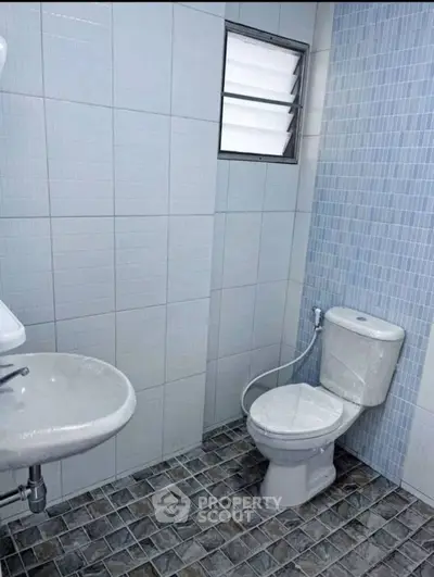 Modern bathroom with tiled walls and floor, featuring a toilet and sink.