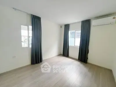 Spacious empty room with wooden flooring and large windows, perfect for customization.
