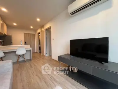 Modern living room with sleek furniture and open kitchen layout, featuring a stylish TV setup and air conditioning.