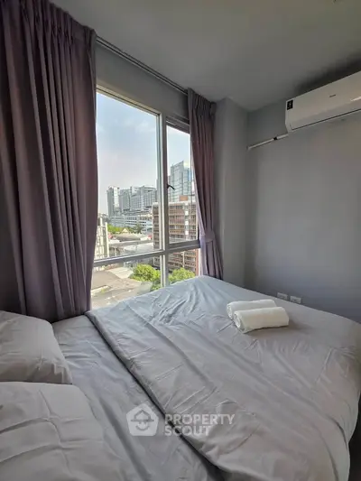 Cozy bedroom with city view, featuring a large window and air conditioning, perfect for urban living.