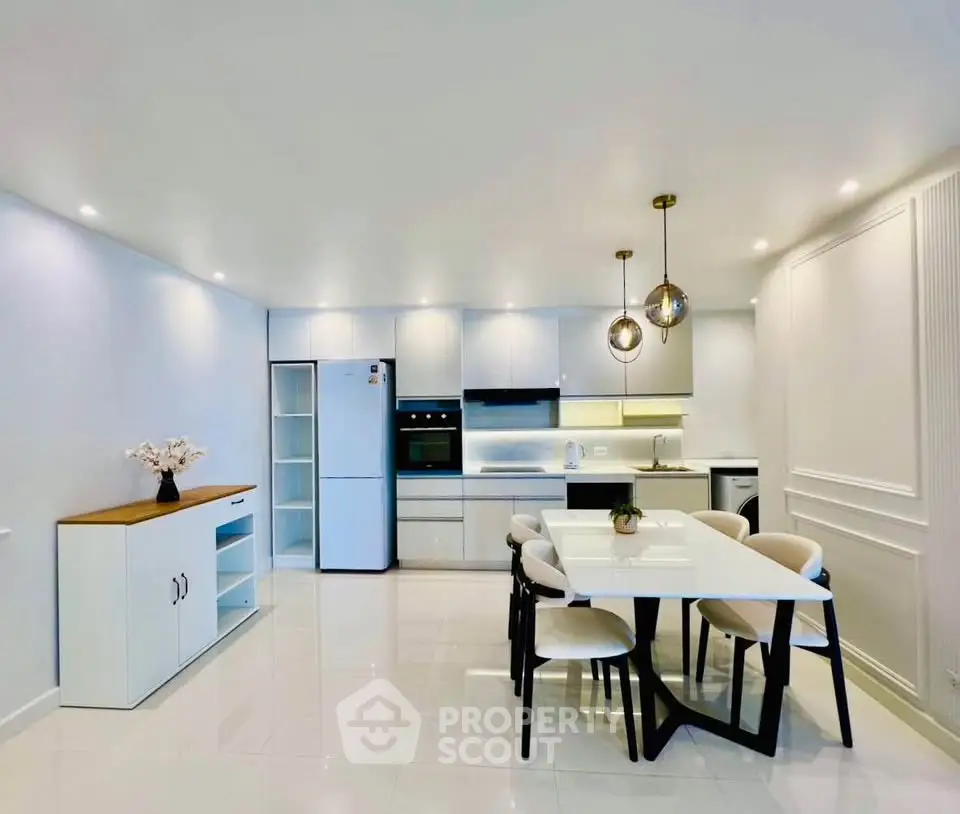 Modern kitchen with sleek white cabinetry, dining area, and stylish lighting fixtures.