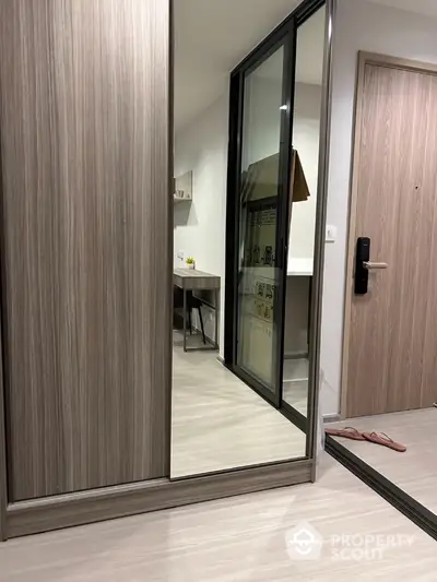 Modern apartment entrance with sleek wooden door and mirrored closet reflecting a cozy interior.