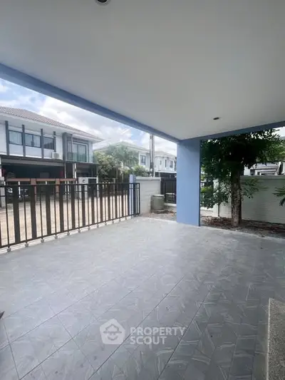 Spacious covered patio with tiled flooring and modern railing in a suburban home.