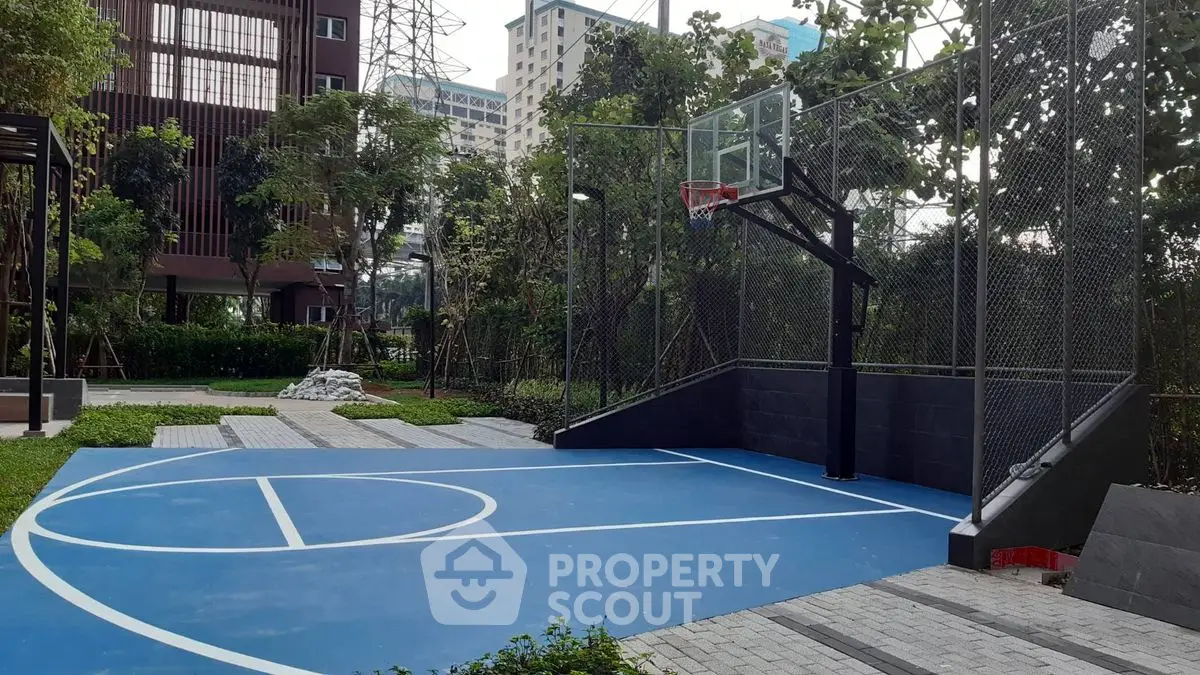 Modern outdoor basketball court in urban residential complex with lush greenery.