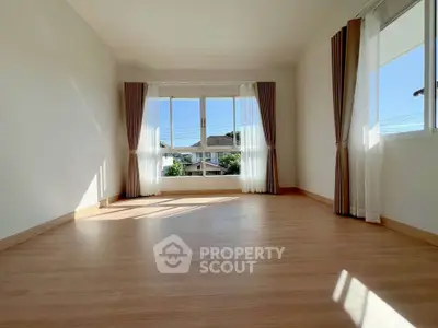 Spacious sunlit room with large windows and elegant curtains, perfect for modern living.
