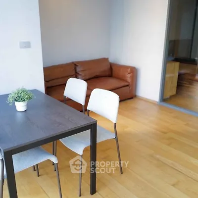 Modern living room with wooden flooring, cozy brown sofa, and sleek dining table with chairs.