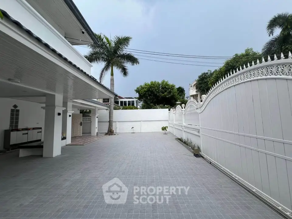 Spacious private driveway with elegant white fencing and tropical palm trees.