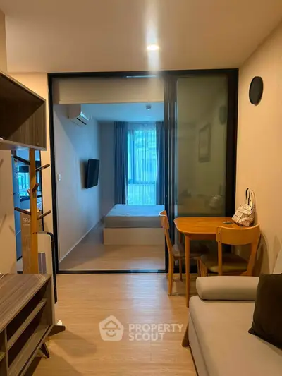 Modern apartment interior with cozy living room and bedroom separated by glass sliding door.
