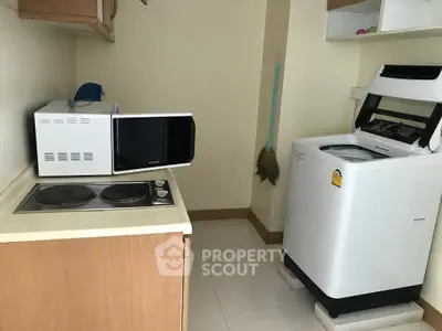 Compact kitchen with microwave, stove, and washing machine in cozy apartment.