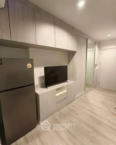 Modern apartment interior with sleek kitchen and TV setup, featuring stylish cabinetry and wood flooring.