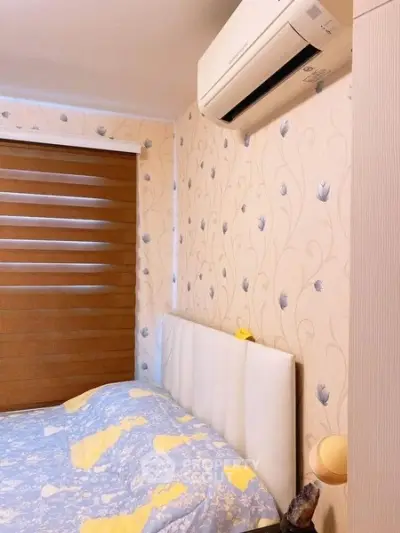 Cozy bedroom with floral wallpaper and air conditioning, featuring a comfortable bed and modern window blinds.