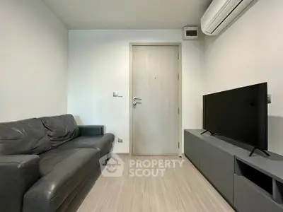 Modern living room with sleek black sofa and flat-screen TV, featuring minimalist design and air conditioning.
