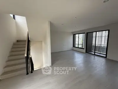 Spacious modern living room with large windows and staircase, perfect for natural light lovers.