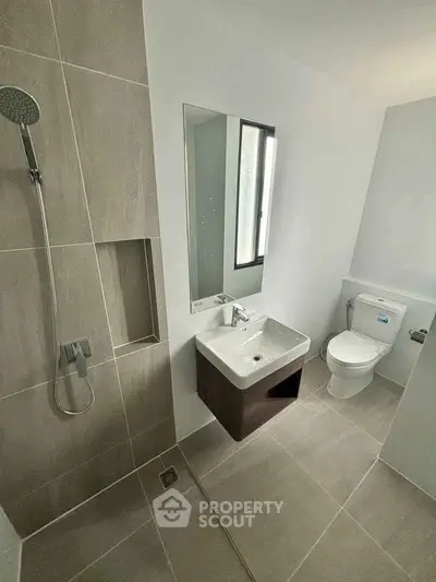 Modern bathroom with sleek fixtures and neutral tiles, featuring a shower and compact sink.