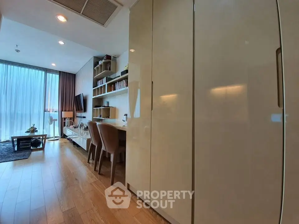 Modern living room with wooden flooring, large windows, and built-in storage.