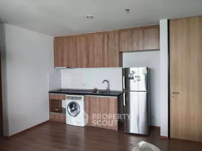 Modern kitchen with wooden cabinets, washing machine, and stainless steel fridge in a sleek apartment.