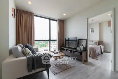 Modern living room with cozy decor and large window offering city view, connected to a stylish bedroom.