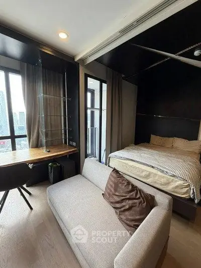 Modern studio apartment with cozy bed, sofa, and city view from large window.