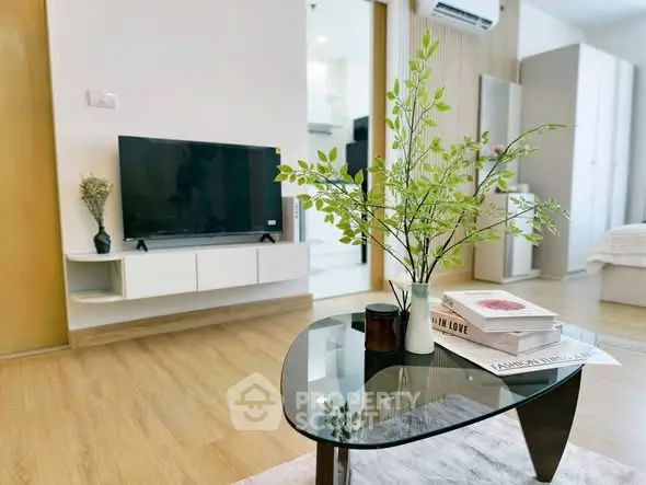 Modern living room with sleek glass coffee table and TV, open to a cozy bedroom.