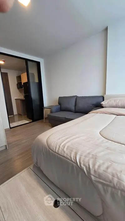 Modern studio apartment with cozy bed and stylish sofa, featuring a sleek open kitchen layout.