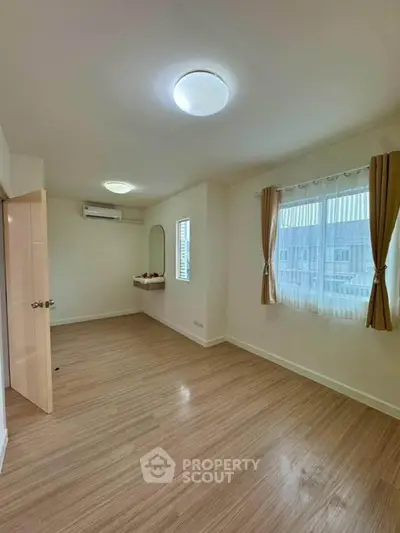 Spacious bedroom with wooden flooring and large window for natural light.
