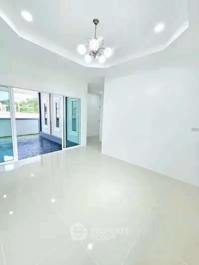 Spacious modern living room with elegant chandelier and large windows opening to a balcony.