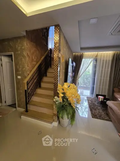 Elegant living room with staircase and floral decor, featuring modern design and natural light.