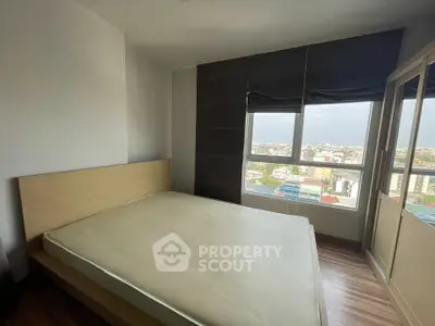 Spacious bedroom with large window offering city views, featuring a modern bed and ample storage space.