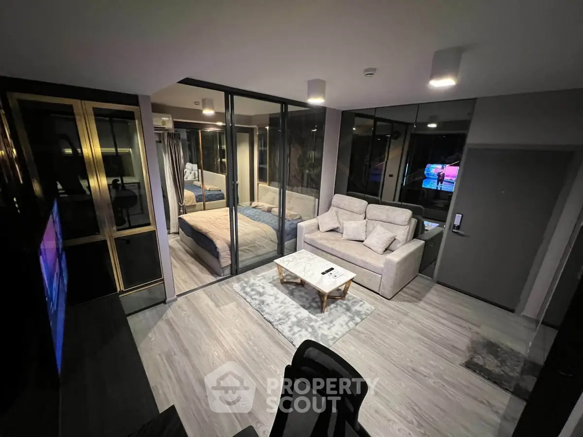 Modern open-plan living room with glass-walled bedroom, stylish decor, and cozy seating area.
