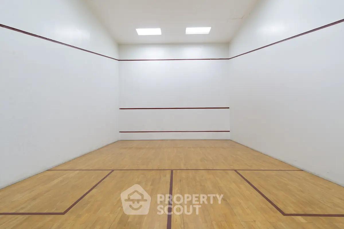 Spacious indoor squash court with wooden flooring and bright lighting, perfect for sports enthusiasts.